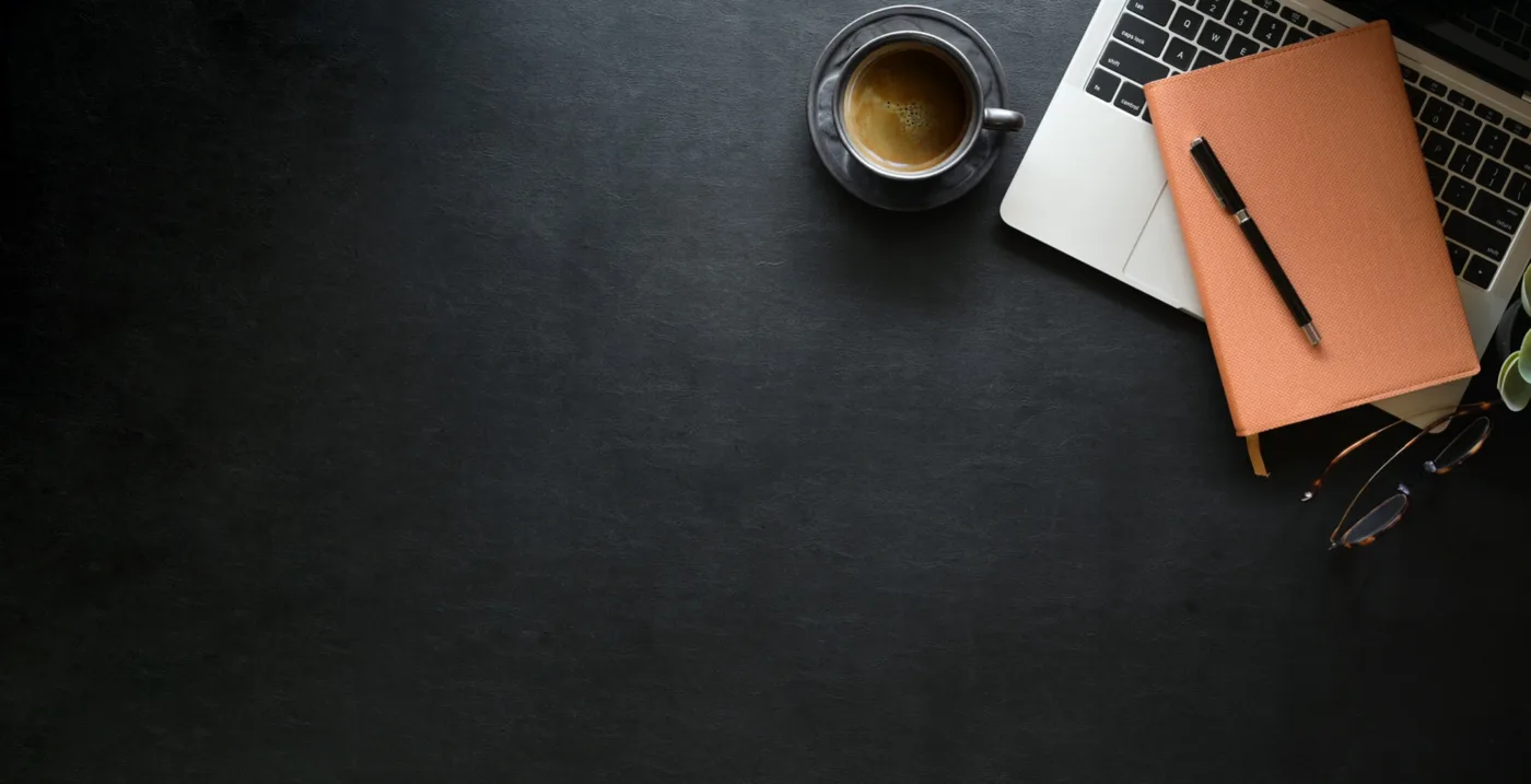 A notebook, coffee and laptop on a dark desk